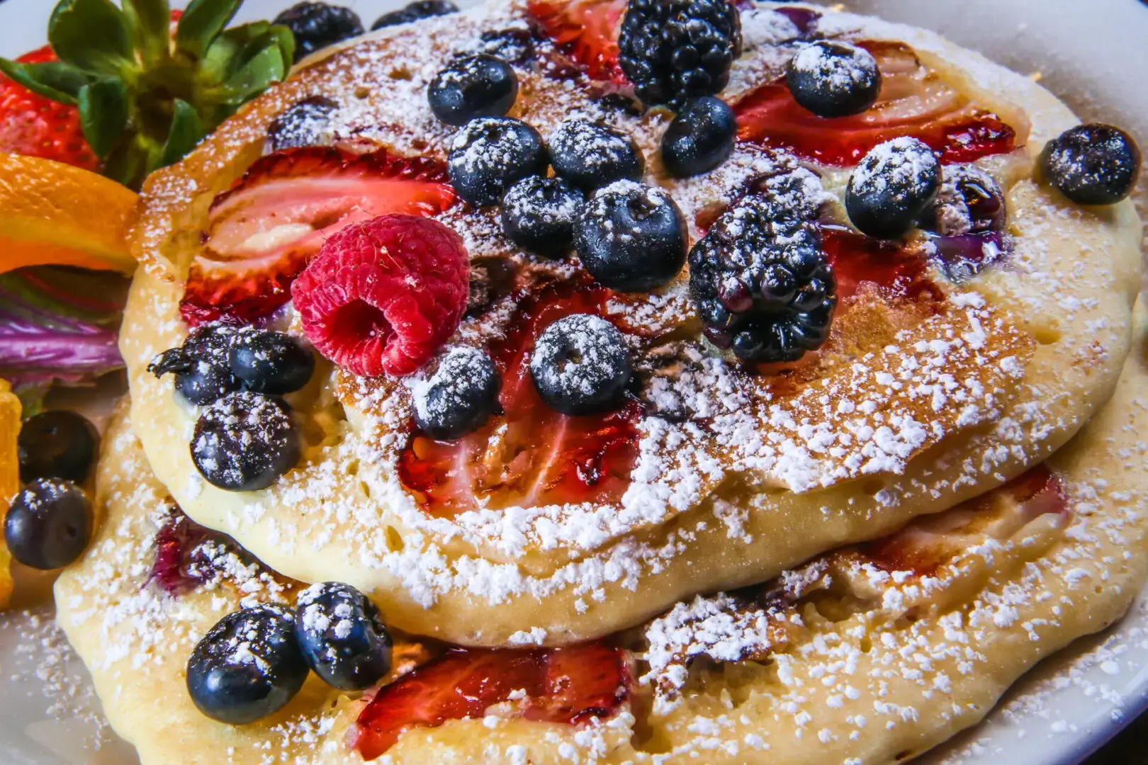 A stack of pancakes with berries and powdered sugar.